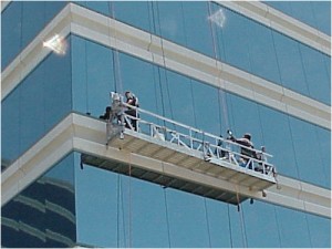 Two window cleansers on suspended scaffolding washing windows on a commercial multistory office facility exterior