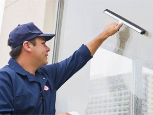 Professional, uniformed window cleaner cleaning an interior office facility window using a squeegee